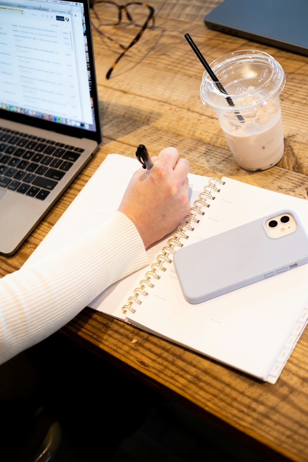 Hands writing a business growth plan in a notebook next to a laptop
